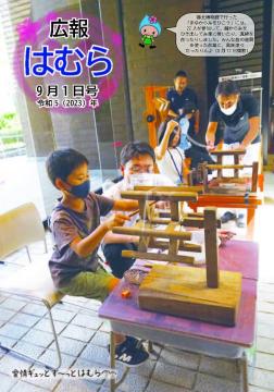 広報はむら9月1日号No.1100表紙　郷土博物館の「まゆから糸をひこう」に参加し糸車で糸をつむぐ体験をする子どもたちの様子