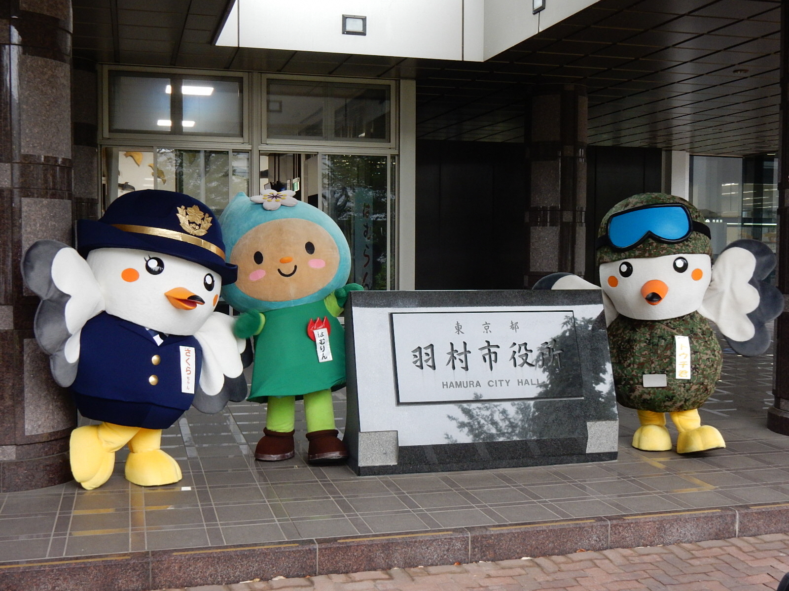 羽村市役所の銘板を囲むさくらちゃんとはむりんとトウチ君