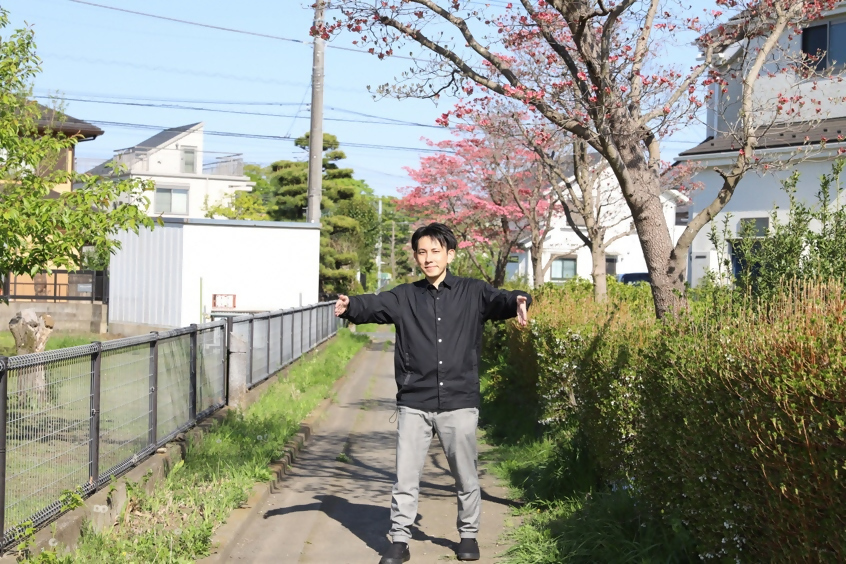 舗装された道の上で手で幅を示す筆者
